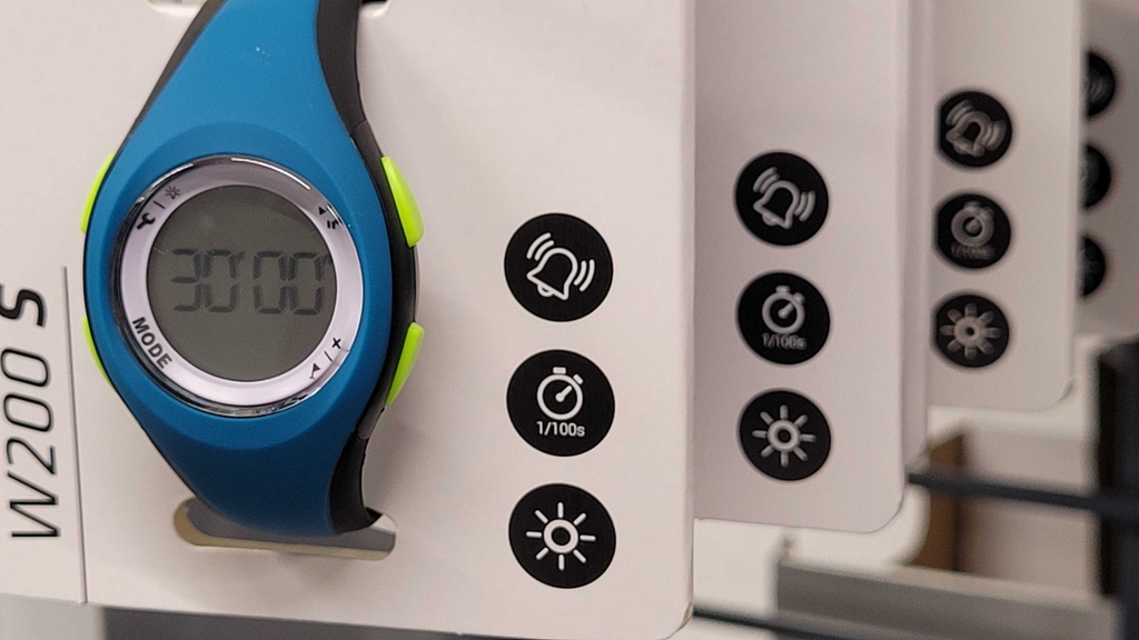 Laufuhr im Test: Detailansicht eines weißen Verpackungskartons mit einer blauen Sportuhr inklusive runder LCD-Anzeige und giftgrüner Tasten.