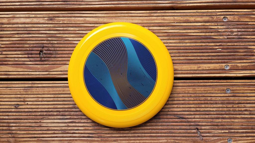 Eine gelbe Frisbee-Scheibe mit blauem Spiraldesign in der Mitte liegt mit der Vorderseite nach oben auf einem Holzuntergrund.