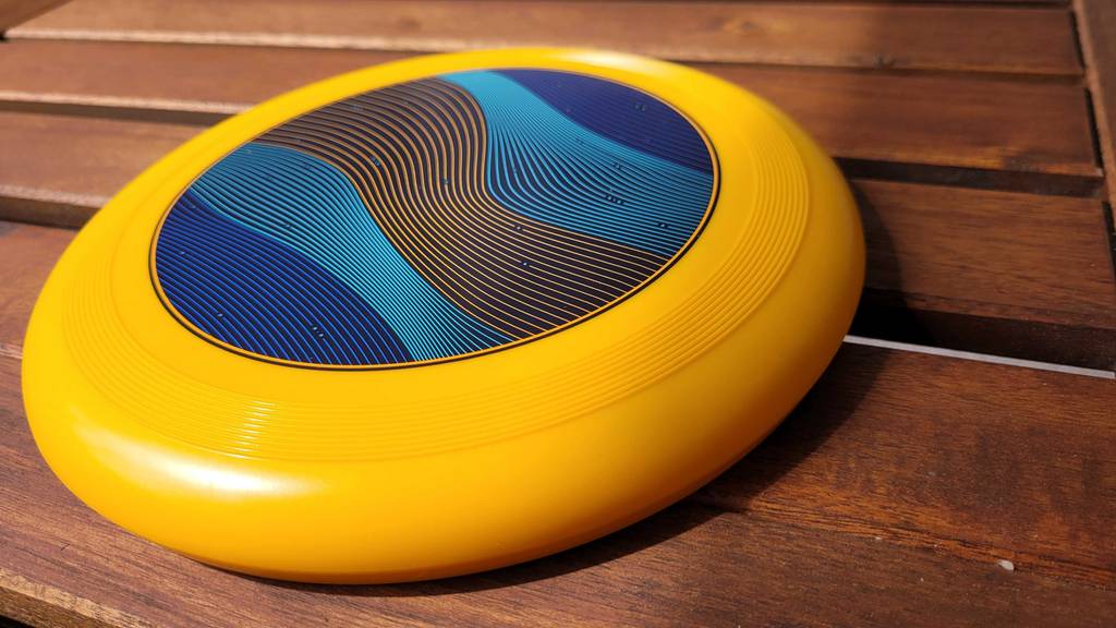 Detailansicht einer getesteten gelben Frisbee Wurfscheibe mit buntem Muster.