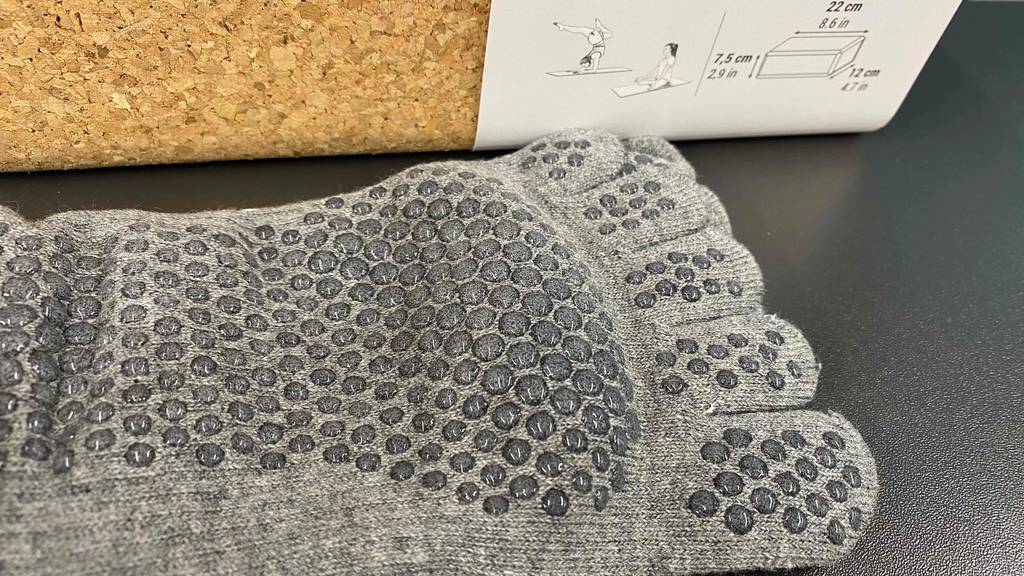 Detailansicht von rutschfesten Gumminoppen auf der Sohle getesteter Yoga-Socken, die vor einem Yogablock aus Kork liegen.