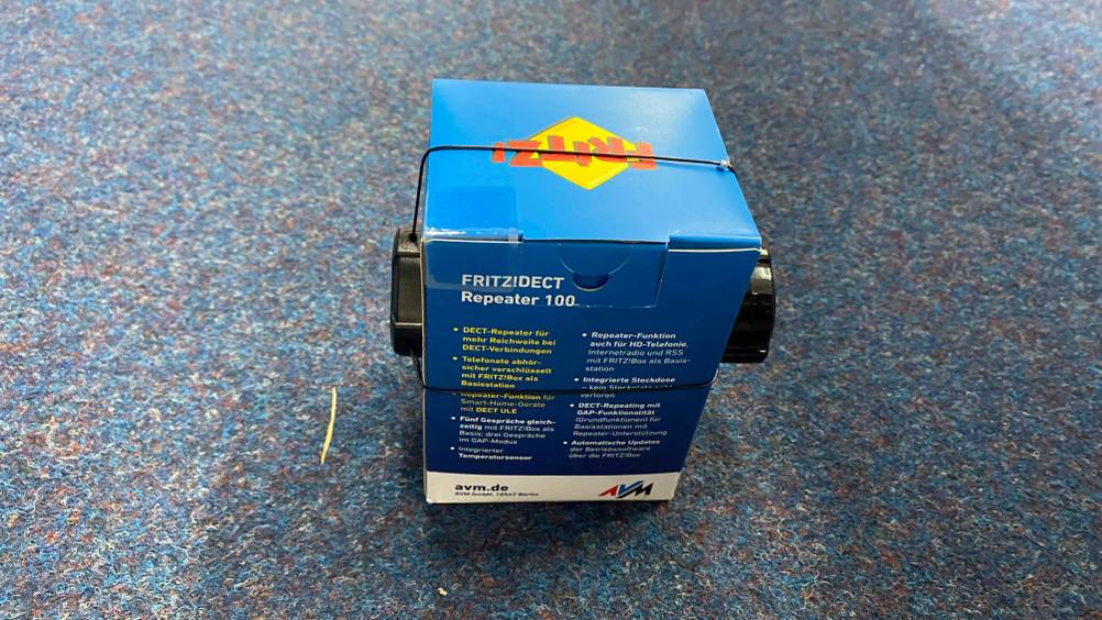 Die Rückseite eines originalverpackten DECT-Repeater im Test auf einem blauen Teppich.