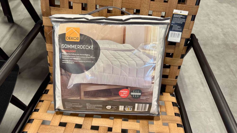 Eine getestete Sommerdecke steht in Verpackungstasche auf einem Flechtstuhl.
