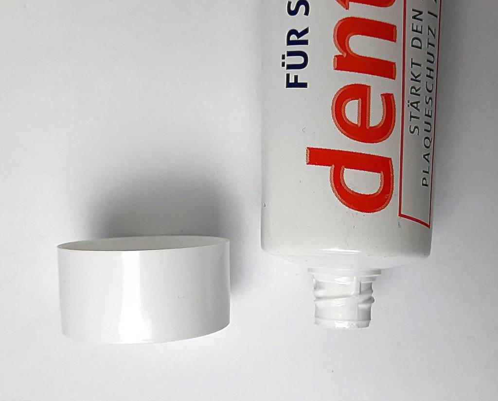 Die Tube mit der remineralisierenden Zahncreme im Test liegt geöffnet neben dem Verschluss auf einer weißen Oberfläche.