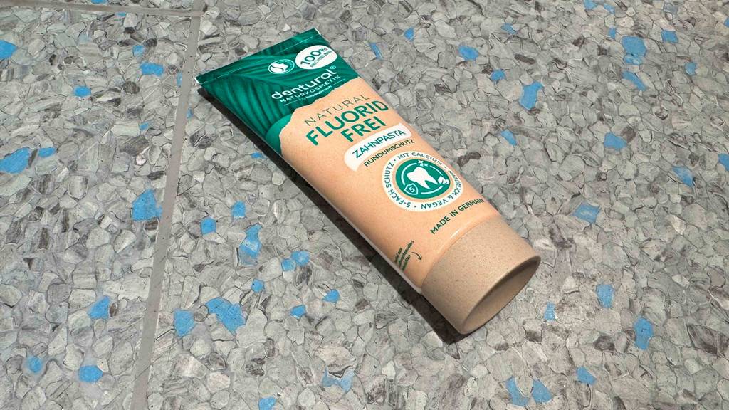 Zahnpasta ohne Fluorid im Test liegt in der Tube auf einem Linoleumbelag.