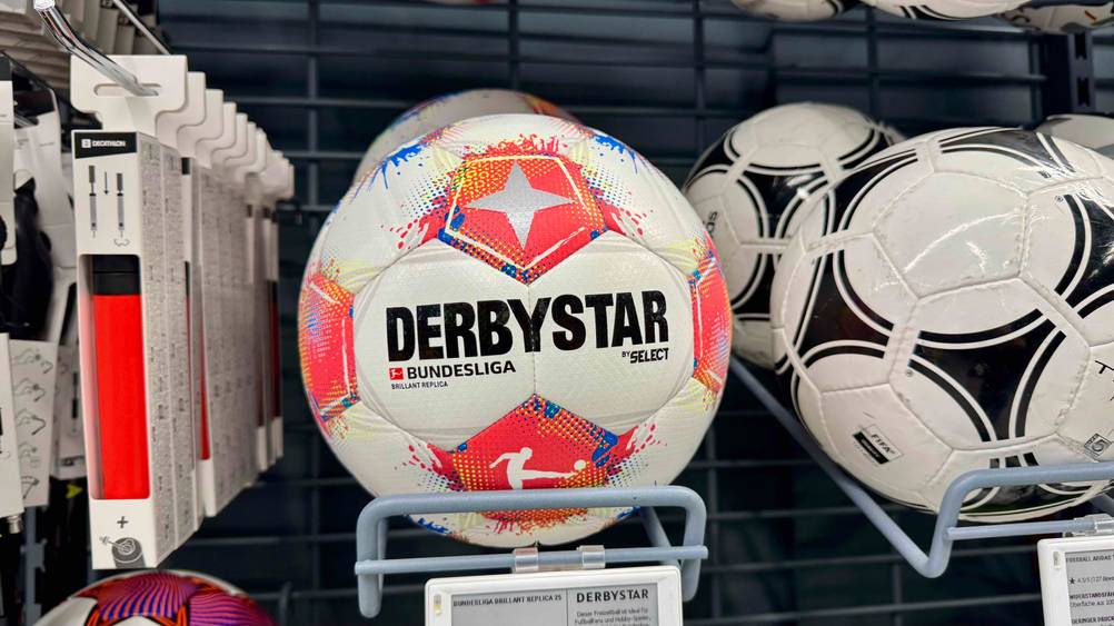 In einem Regal befinden sich mehrere der getesteten Derbystar-Fußbälle neben anderen Produkten.