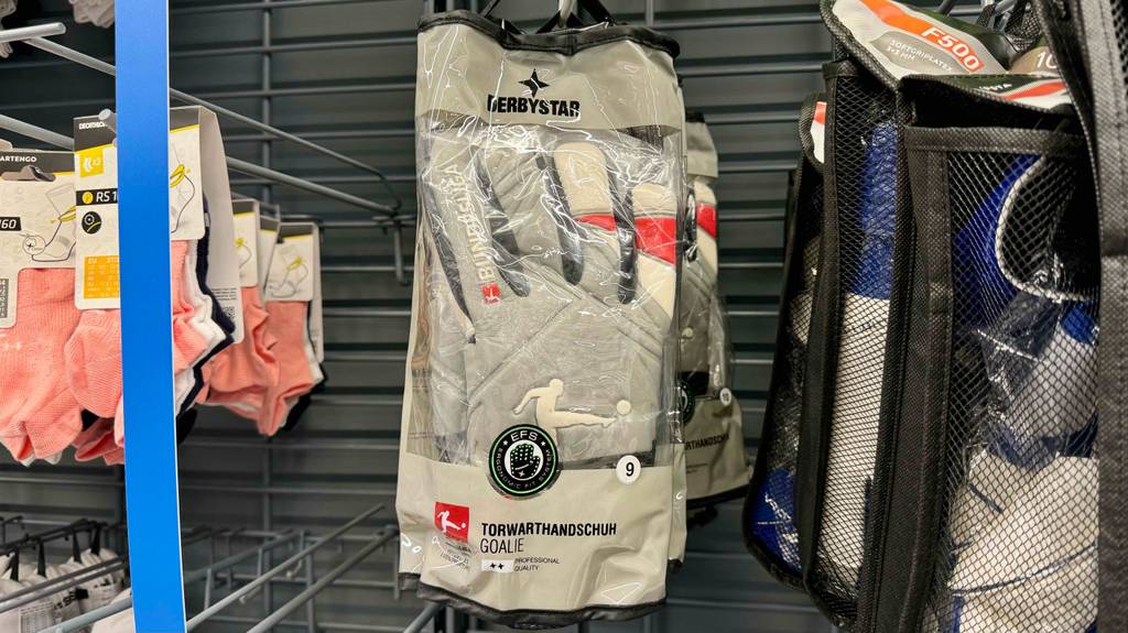 Torwarthandschuhe in Originalverpackung hängen zum Testen zwischen anderen Produkten in einem Regal.