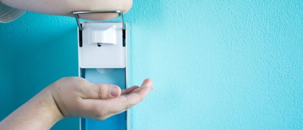 Desinfektionsspender im Test: Jemand betätigt einen Desinfektionsspender an der Wand mit dem Ellenbogen.