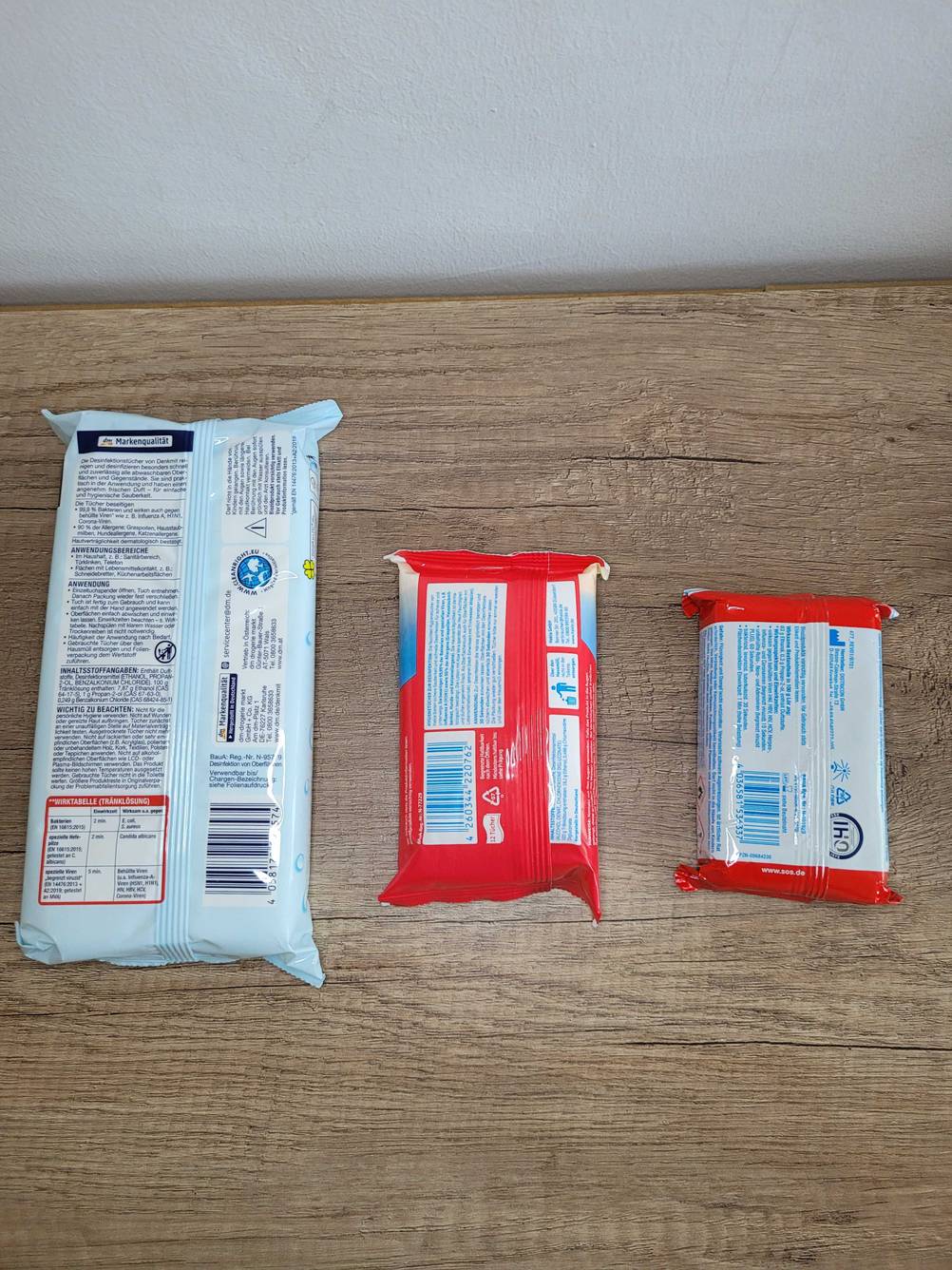 Desinfektionstücher getestet: Drei unterschiedliche Packungen liegen mit der Rückseite nach oben auf einer Holzfläche.