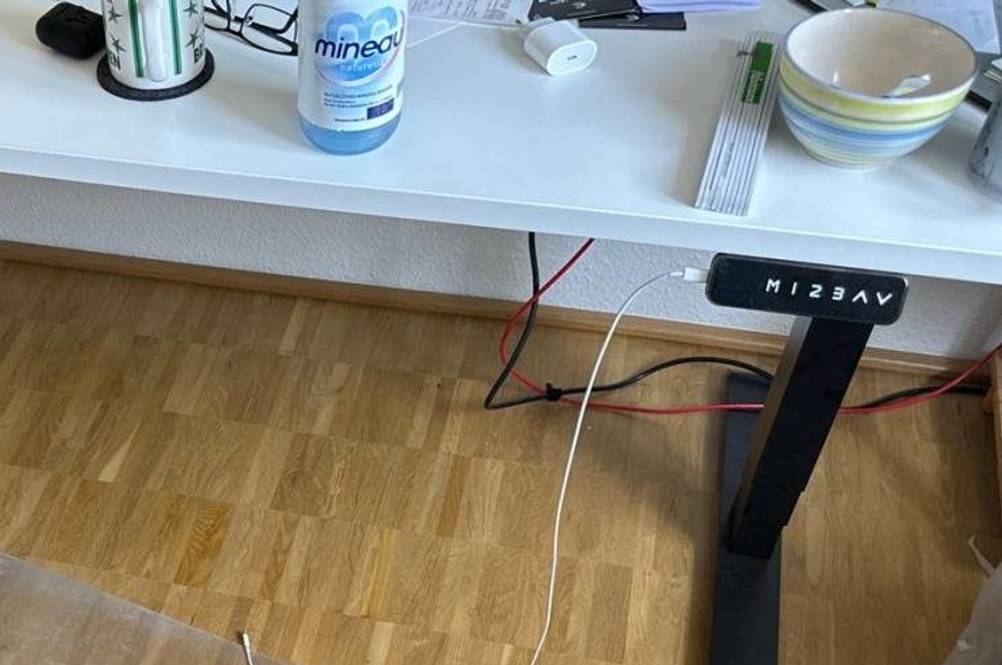 Höhenverstellbarer Schreibtisch mit schwarzem Gestell und weißer Tischplatte steht auf einem Holzboden mit USB-Ladung.