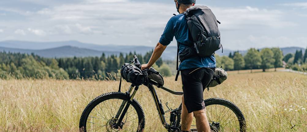 Deuter-Tagesrucksack-Test: Mann mit seinem Fahrrad und Rucksack auf einer Wiese.