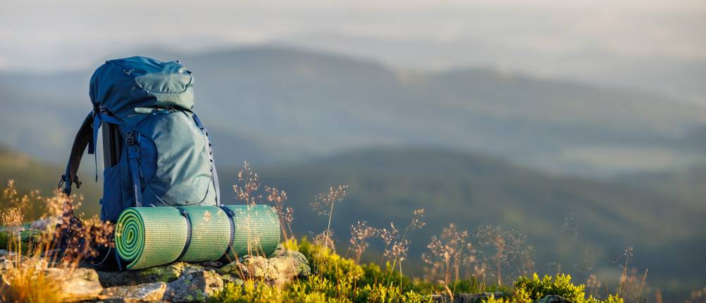 Deuter-Tagesrucksack-Test: Wanderrucksack mit Isomatte steht in der freien Natur mit Blick auf ein Bergpanorama.