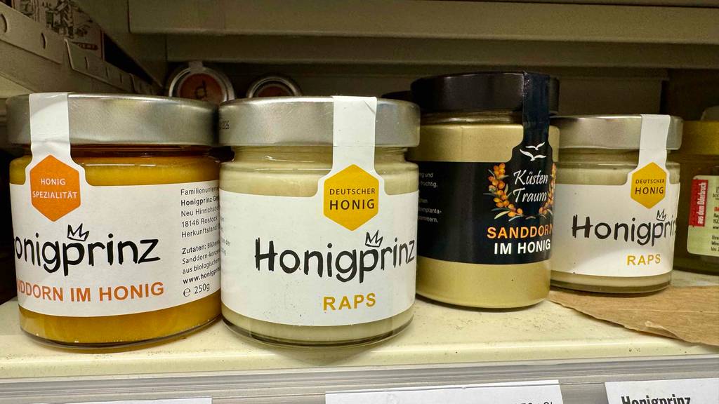 Getestet: Honigprinz Raps im Glas steht auf einem Regal neben verschiedenen Honigsorten.