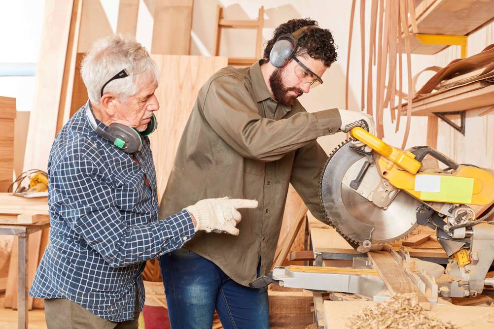 DeWalt-Kappsäge im Test: Ein älterer Mann weist einen jüngeren Mann bei der Arbeit an der Säge ein.