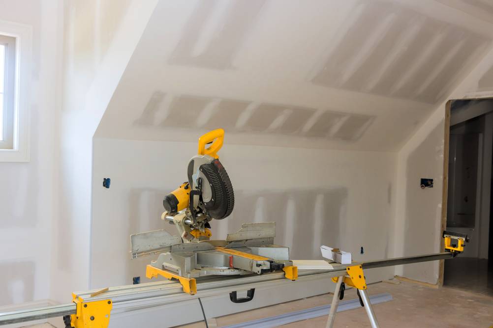 DeWalt-Kappsäge im Test: Ein Untergestell mit Säge und Verlängerungsschienen in einer Baustelle, wobei frisch erstellten Rigipswände zu erkennen sind.