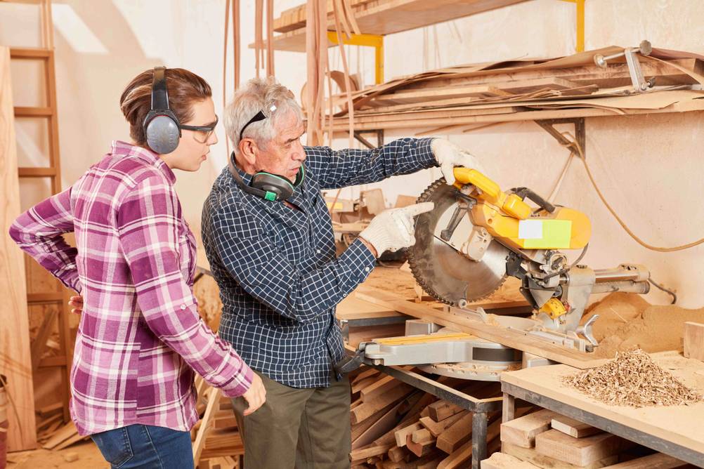 DeWalt-Kappsäge im Test: Ein älterer Mann und eine junge Frau stehen vor einer Säge. Der Mann erklärt etwas zum Werkzeug.