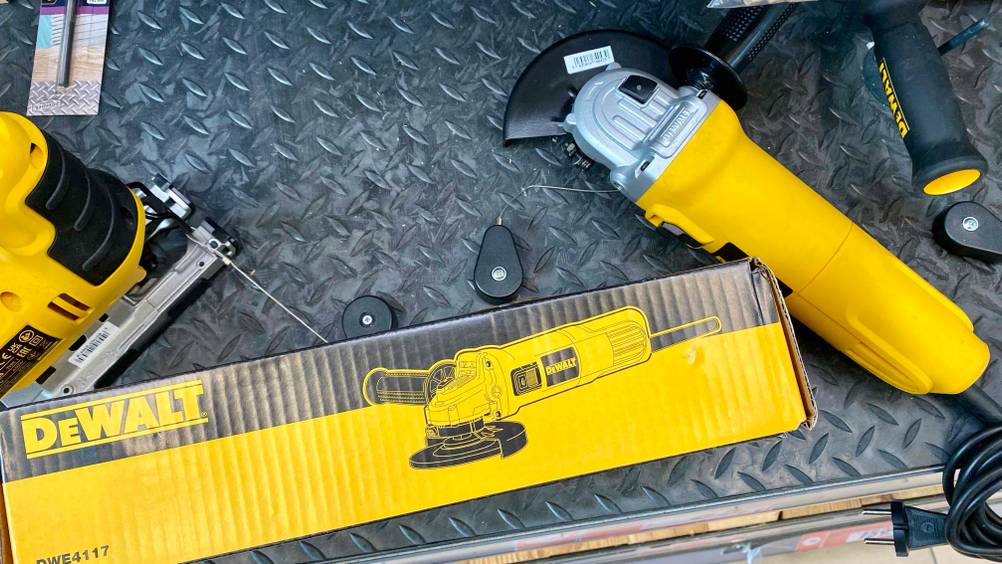 Nahaufnahme der Grafik auf der Verpackung eines getesteten DeWalt-Winkelschleifers, daneben das Gerät auf einer dunklen Fläche.