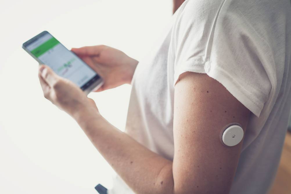 Eine Diabetikerin mit einem Blutzuckersensor checkt ihre Blutzuckerwerte auf dem Smartphone.