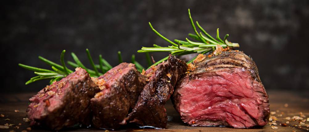 Dickes Fleischstück, das medium gegrillt wurde, liegt auf einem Holzbrett vor einem dunkeln Hintergrund.