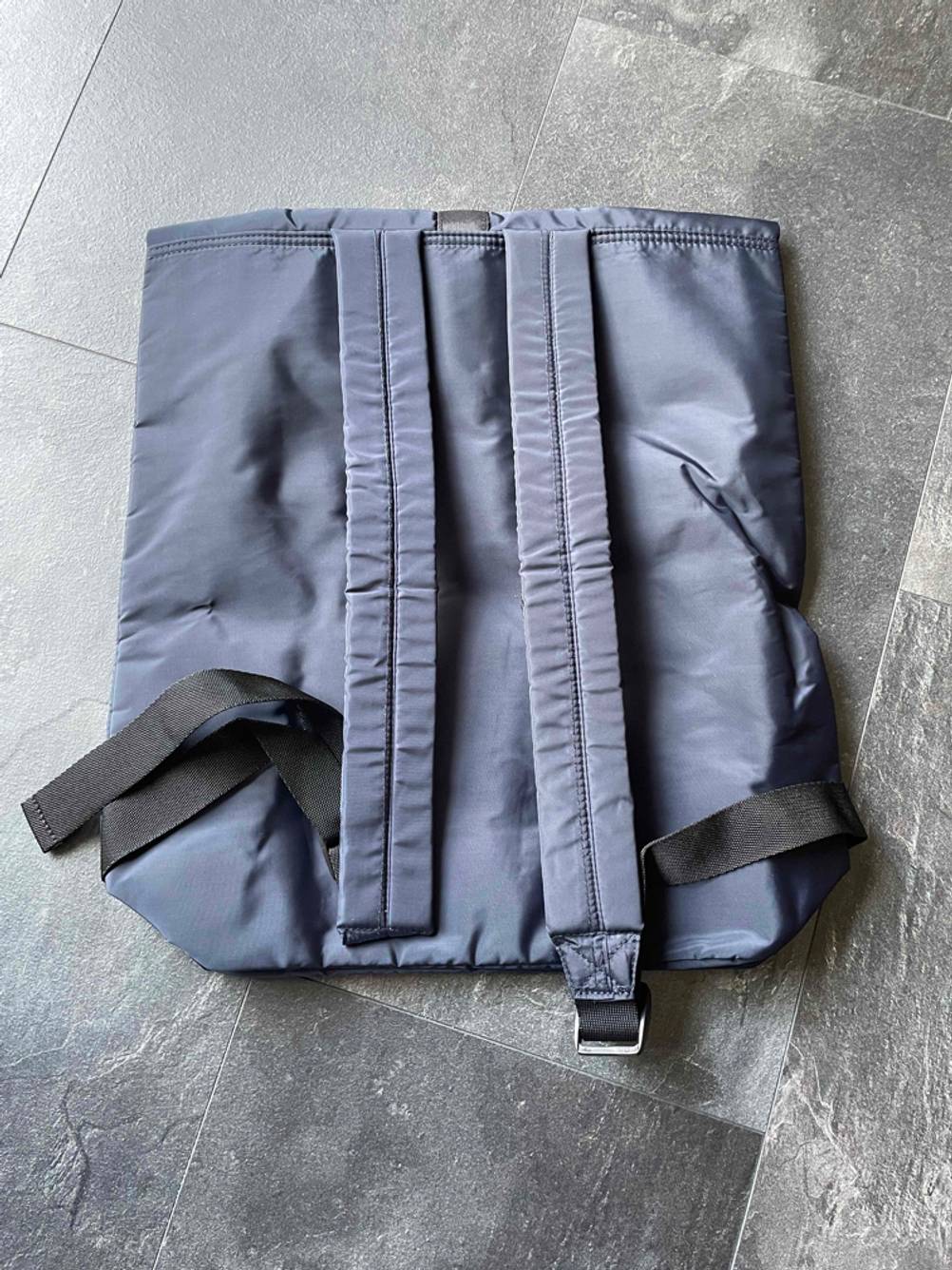 Ein getesteter Roll Top Rucksack liegt flach mit den Trägern nach oben auf einem Fliesenboden.