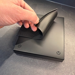 Eine Hand zieht eine Gummiauflage von der digitalen Timemore-Kaffeewaage