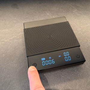 Ein Finger drückt etwas auf der digitalen Timemore-Kaffeewaage