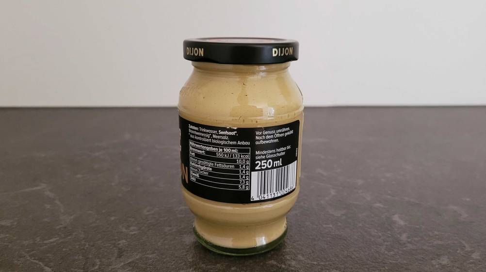 Die Rückseite eines Glases des getesteten Dijon-Senf auf einer dunklen Fläche.