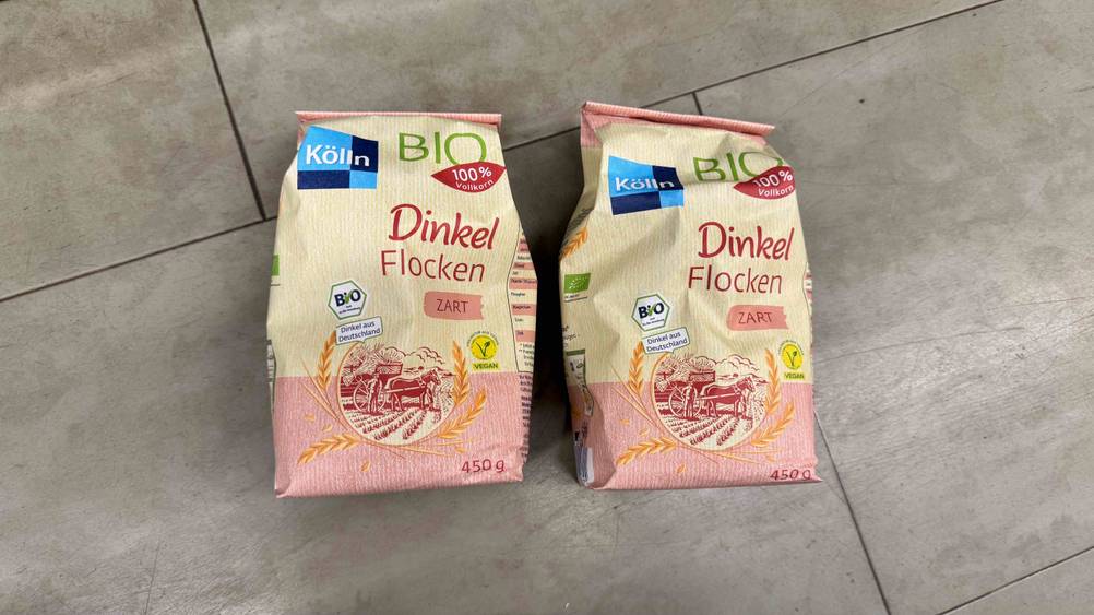 Auf einem grauen Boden liegen zwei Packungen der getesteten Dinkelflocken.