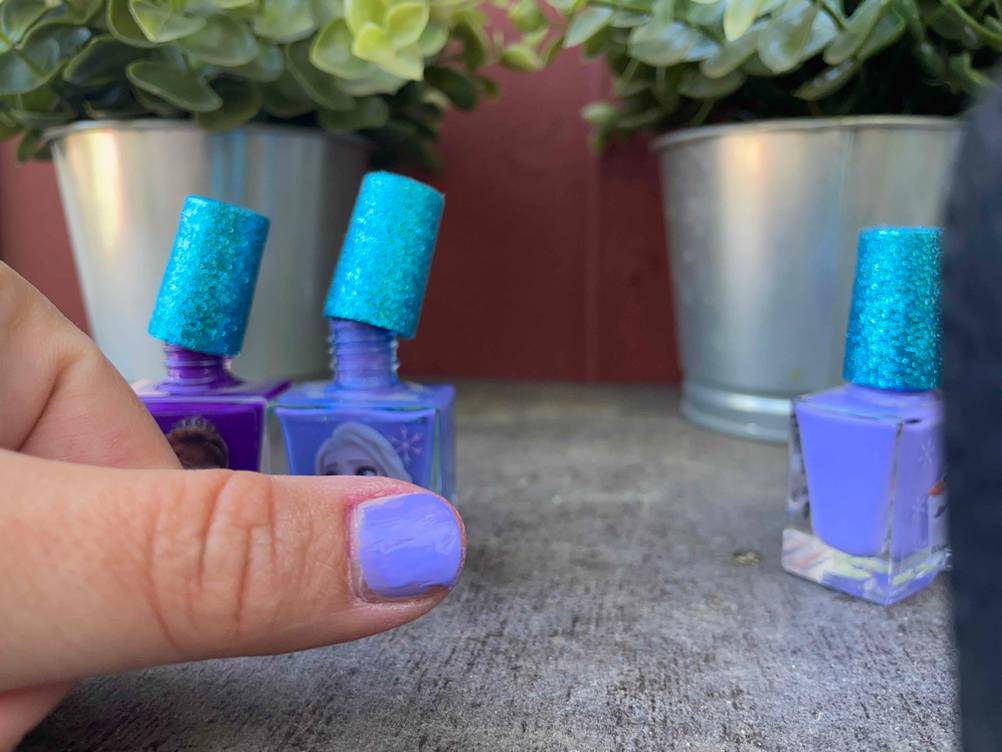 Nagellack für Kinder getestet: Ein lackierter Nagel mit drei geöffneten Fläschchen im Hintergrund.