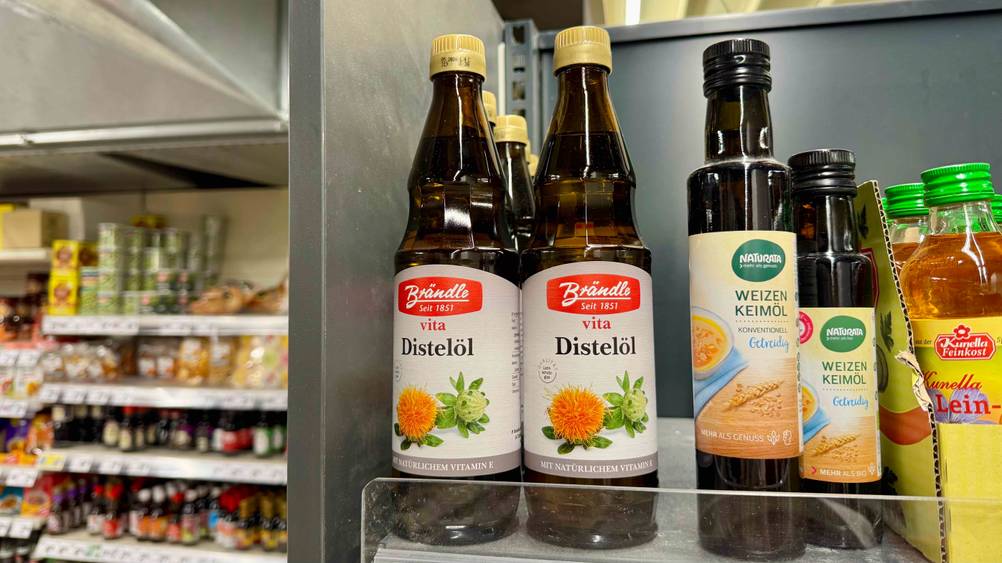 Mehrere Flaschen des getesteten Distelöls stehen in einem Verkaufsregal neben anderen Produkten.