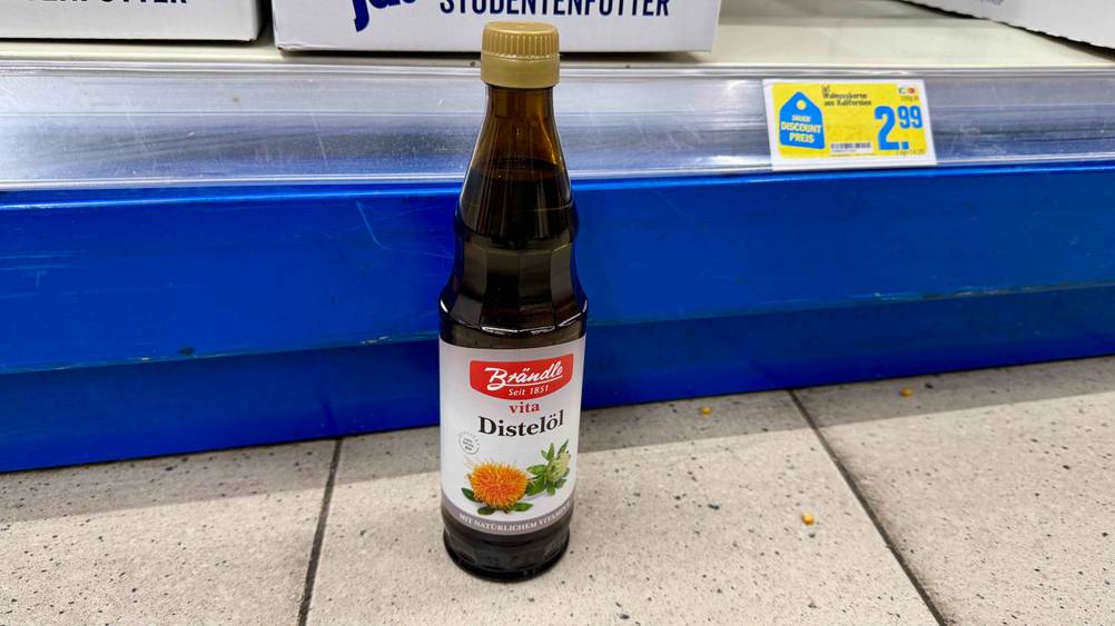 Ein Distelöl im Test vor einem Regal mit Preisschild stehend.