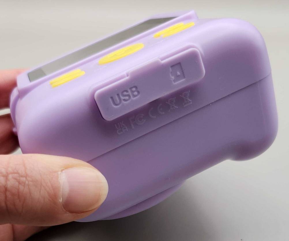Eine Hand hält die getestete Kinderkamera, mit Fokus auf den USB-Anschluss, über einer weißen Fläche.