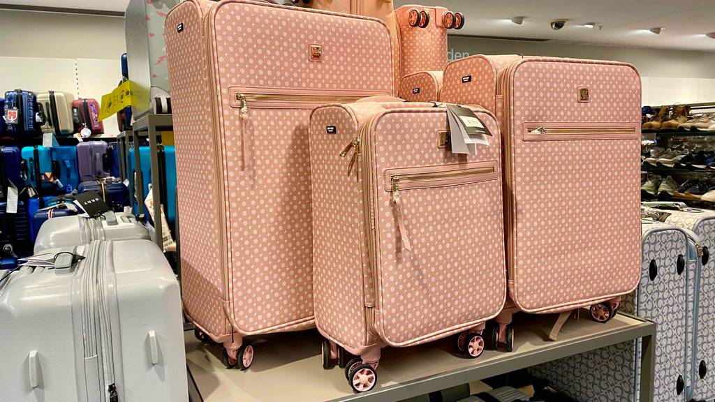 Rosafarbenes getestetes 3-teiliges Kofferset steht in einem Geschäft auf einem Regal neben weiteren Koffern.