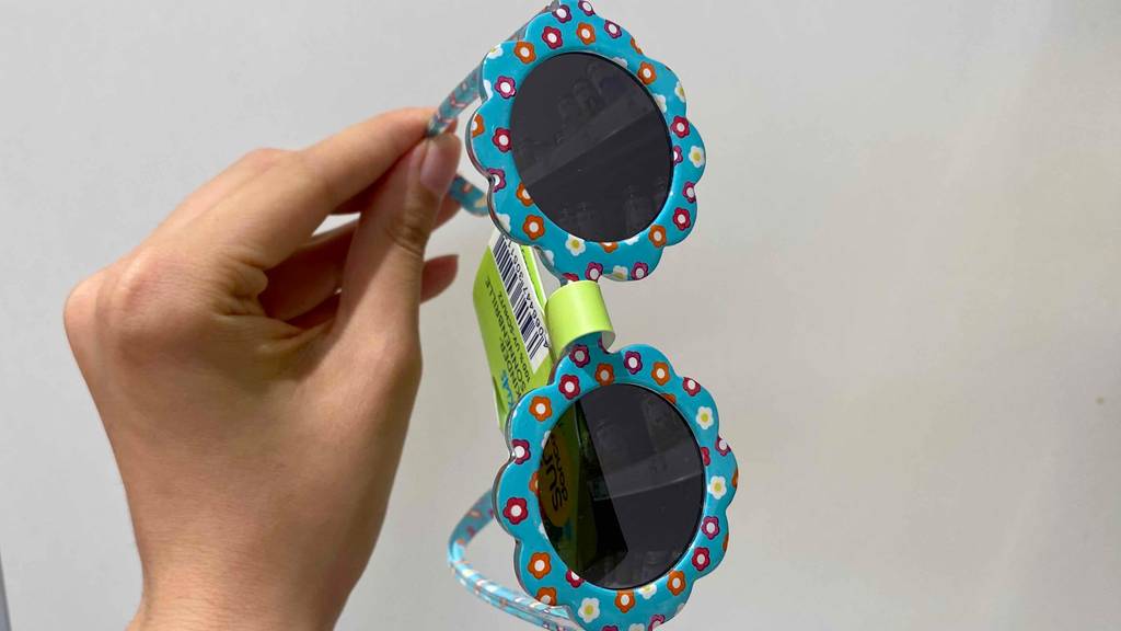 Hand hält eine getestete Babysonnenbrille vor einen weißen Hintergrund.