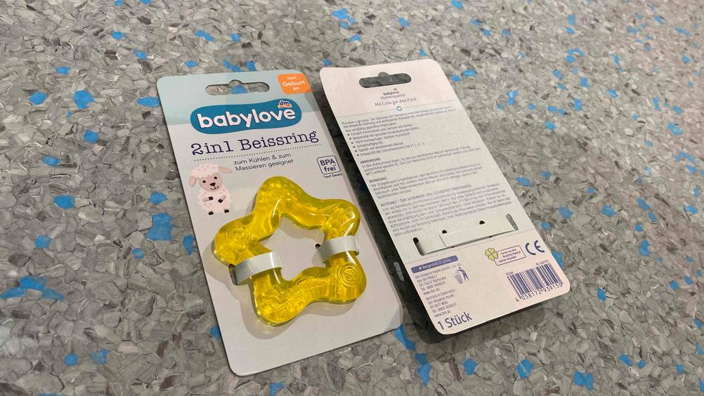 DM-Babylove-2in1-Beißring im Test: Gelb-transparenter Beißring in seiner Verpackung, die von vorn und von hinten inklusive Produktbeschreibung zu sehen ist.