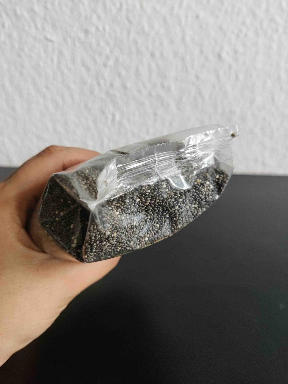 Chia-Samen getestet: Boden einer Packung Chia-Samen von einer Hand vor eine Wand gehalten.