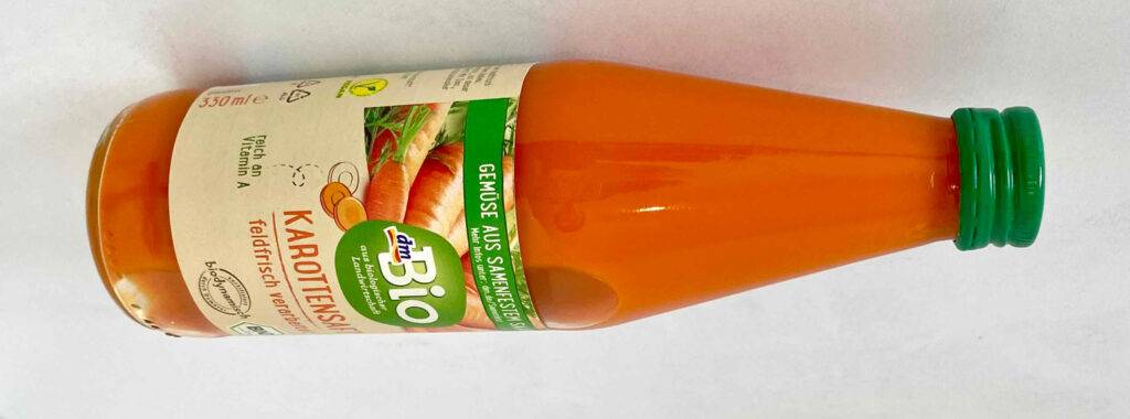 Gesamtansicht einer 330-ml-Glasflasche mit Karottensaft im Test, die auf einer weißen Oberfläche liegt.