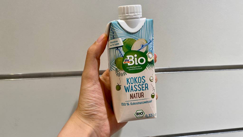 Bio Kokoswasser von DM im Test: eine Hand hält ein Tetrapack vor einem hellen Hintergrund.