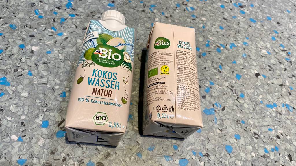 Getestet: Zwei Packungen Bio Kokoswasser von DM liegen nebeneinander auf gesprenkeltem Hintergrund, eine davon mit Ansicht der Rückseite.