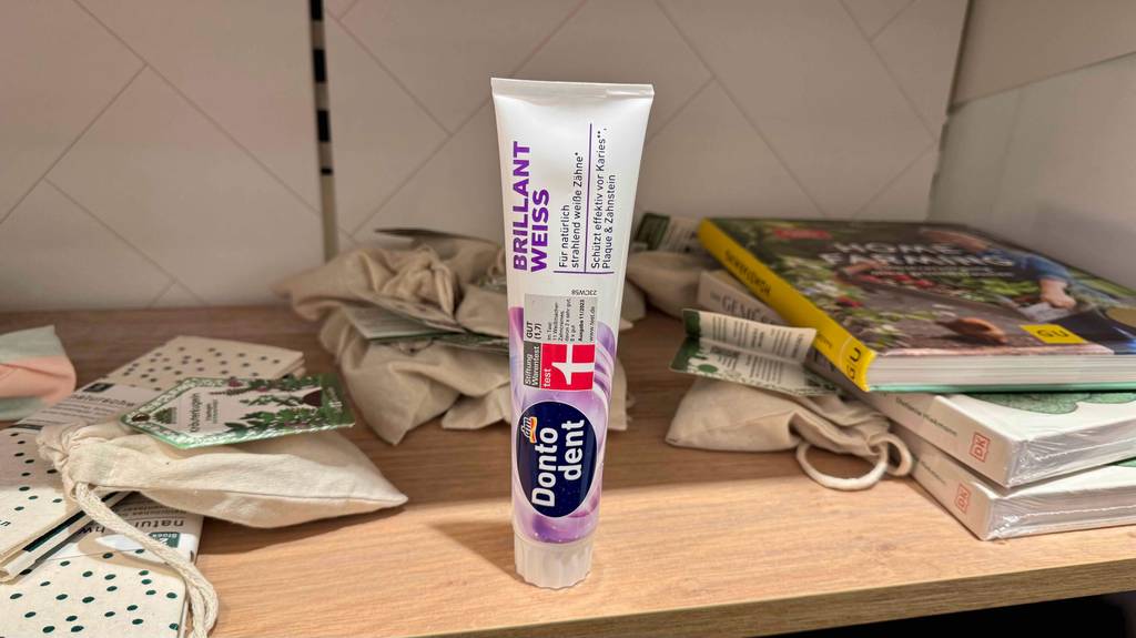 Eine getestete Zahnpasta für weiße Zähne steht in ihrer Tube auf einem Bücherregal.