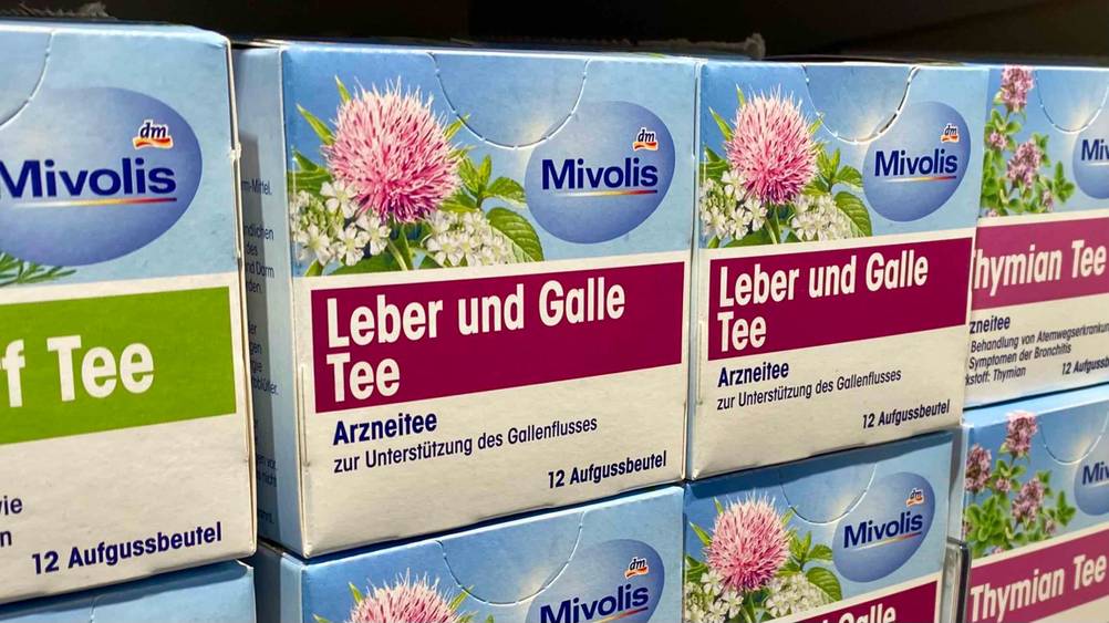 Mehrere getestete Packungen Lebertee neben anderen Produkten im Regal.