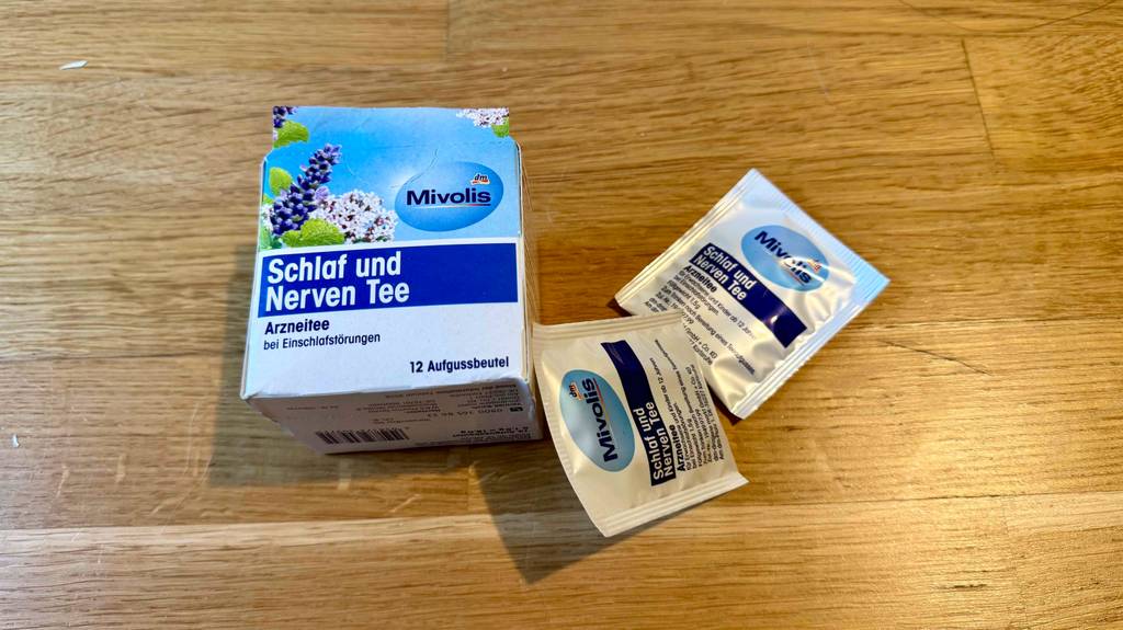 Schlaf-und-Nerventee getestet: Die Aufbewahrungsbox für 12 Beutel liegt auf einer Holzfläche mit einem anlehnenden und einem danebenliegenden Teebeutel.