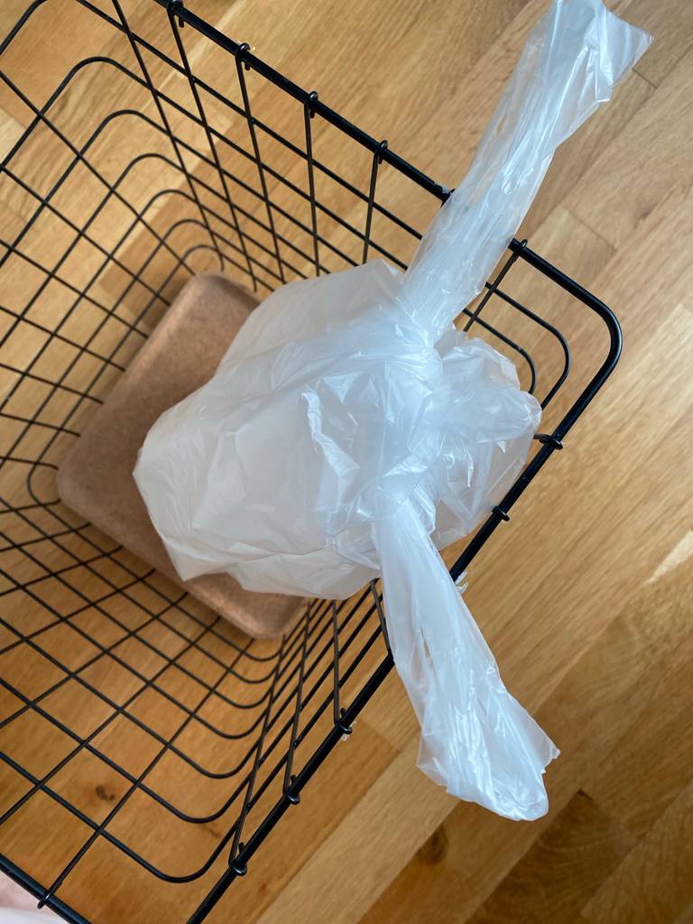 Ansicht von oben auf einen transparenten, getesteten Müllbeutel, der sich zugeschnürt in einem Müllkorb befindet.