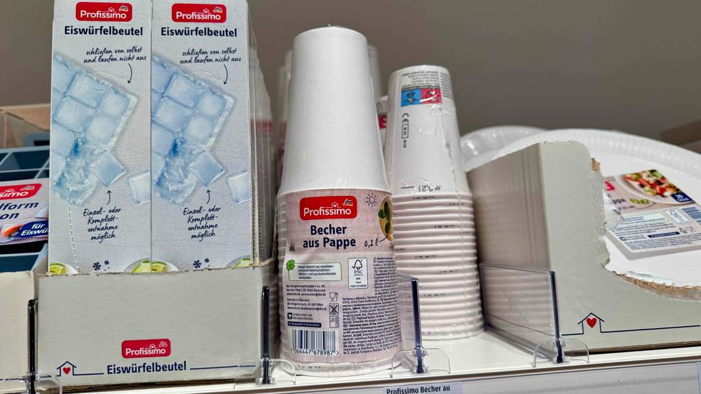 Einwegbecher im Test: Mehrere Packungen stehen zwischen anderen Produkten.