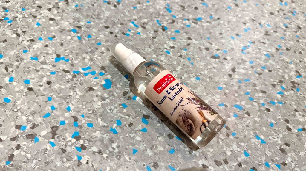 Eine Flasche mit getestetem Kissenspray liegt quer auf einem gesprenkelten Boden.