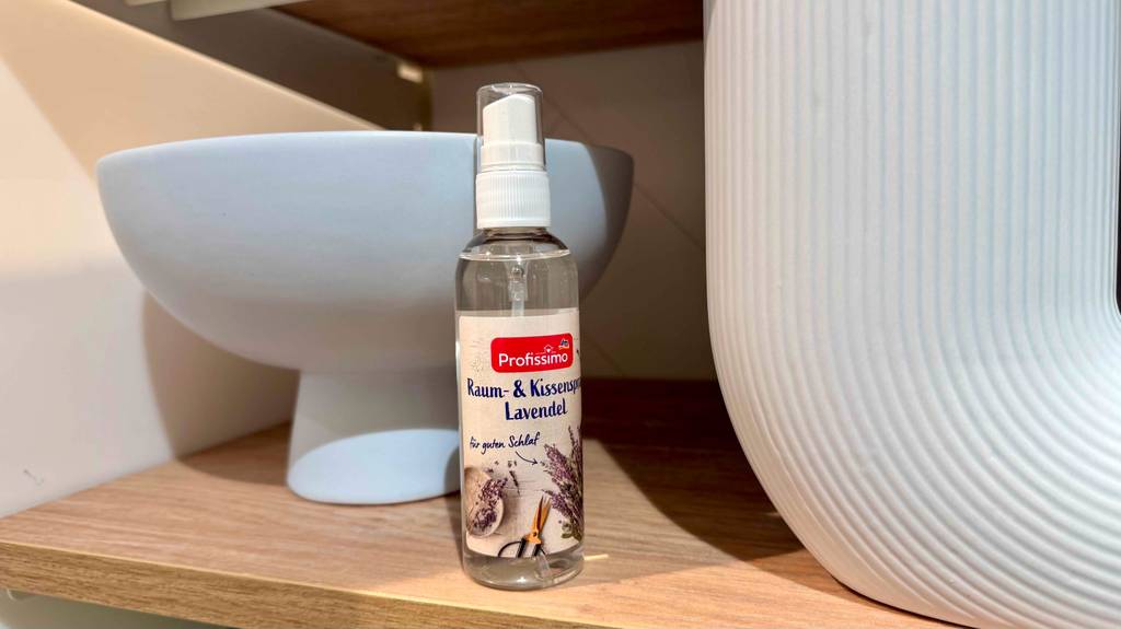 Eine Flasche Kissenspray steht zum testen in einem Holzregal vor Keramik.