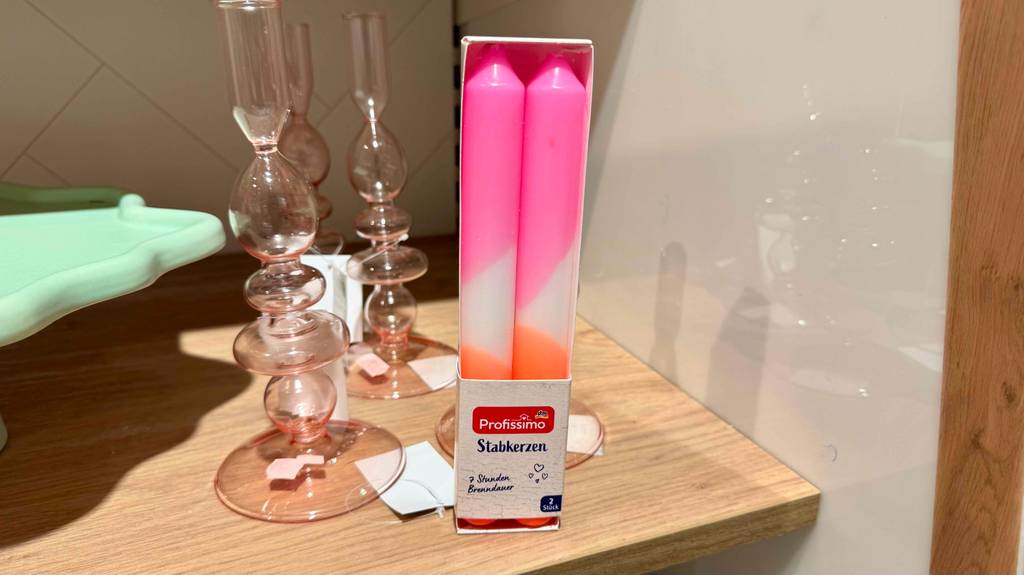 Eine Packung mit Stabkerzen steht zum testen neben Glaskerzenhaltern.