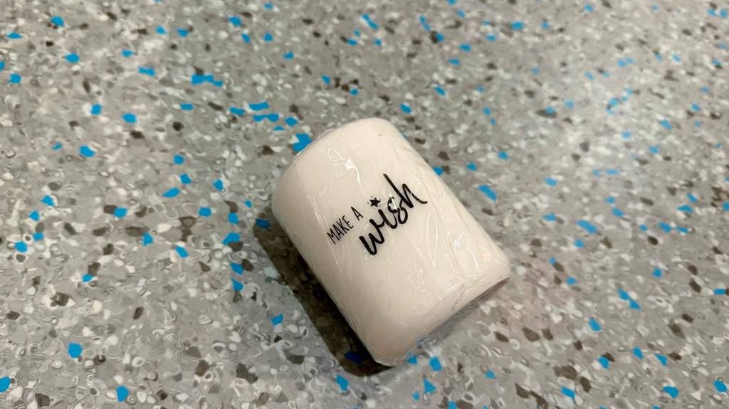 Eine getestete weiße Stumpenkerze mit Schriftzug liegt auf einem Boden.
