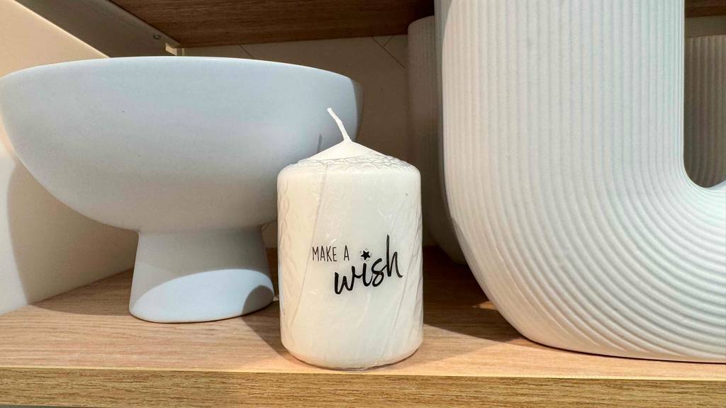 Stumpenkerzen getestet: Eine Kerze mit dem Spruch Make a Wish steht vor Keramik in einem Holzregal.
