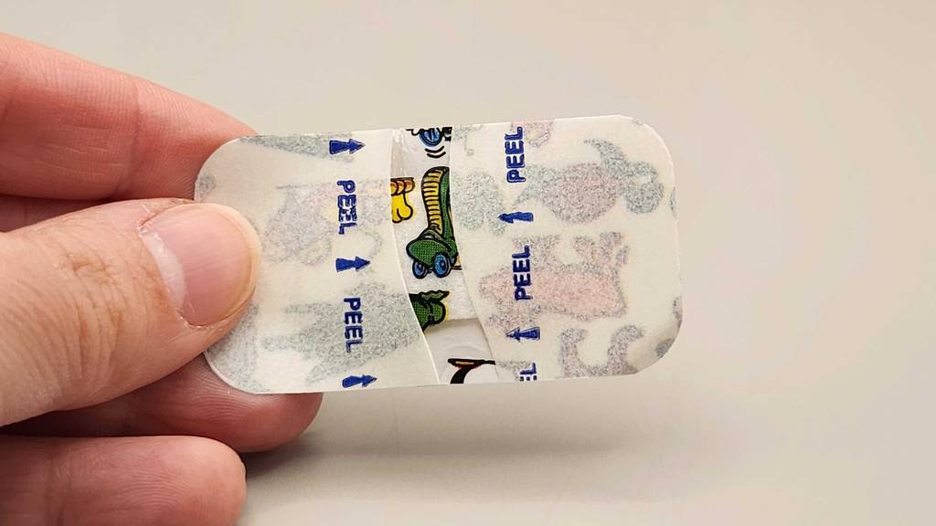 Mehrere Finger halten ein ausgepacktes Kinderpflaster im Test.
