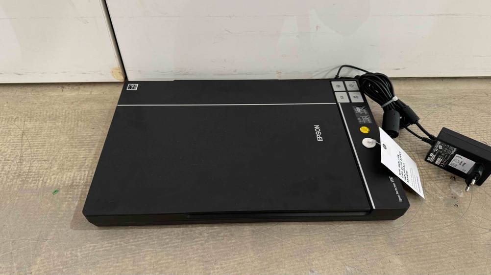 Getestet: Ein Dokumentenscanner von schräg oben mit geschlossener Klappe und Stromkabel auf einem beigen Boden.